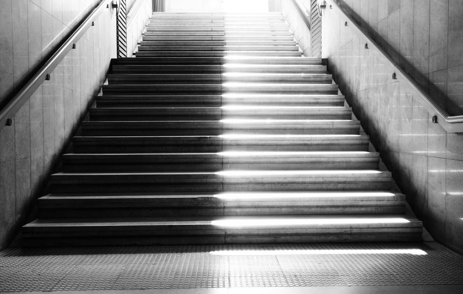 Un escalier de béton vu de face, un rai de lumière posé en son milieu de la première à la dernière marche